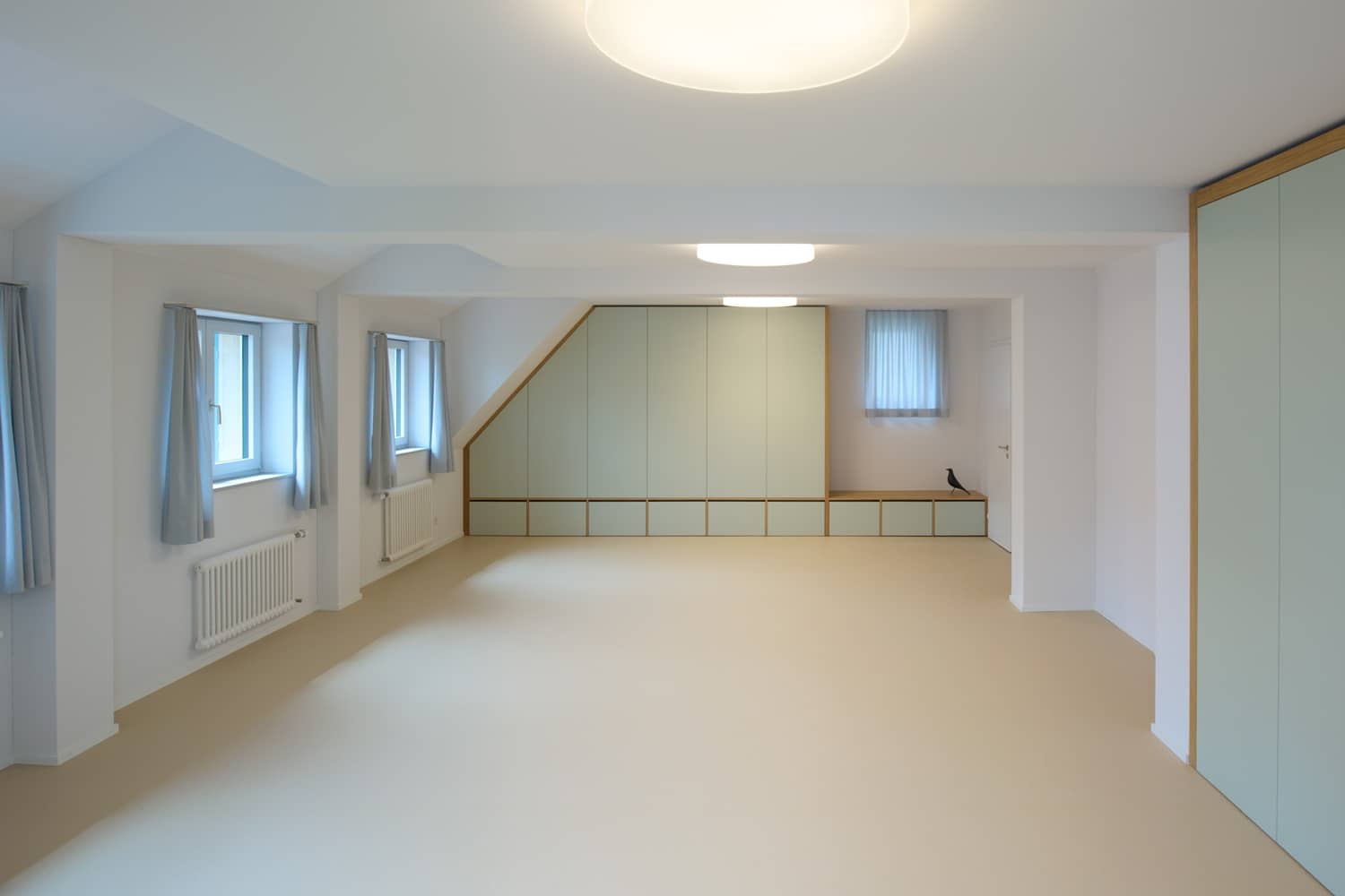 Ein leerer Raum wird mit Licht durchflutet, welches von den Leuchten und der Fensterfront kommt